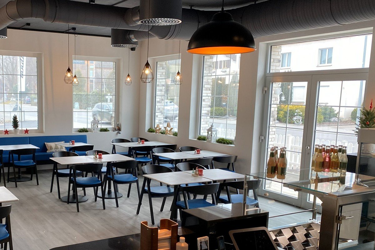 Das helle Restaurant von innen, mit Holzboden, blauen Stühlen und grossen Fenstern